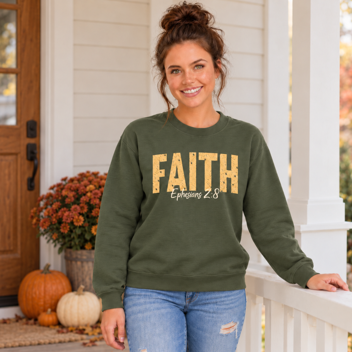 Woman modeling a military green crewneck sweatshirt with distressed gold FAITH text and white Ephesians 2:8 script near fall pumpkins and mums.