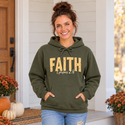 Woman wearing a military green pullover hoodie with distressed gold FAITH lettering and white Ephesians 2:8 script on a decorated fall porch.