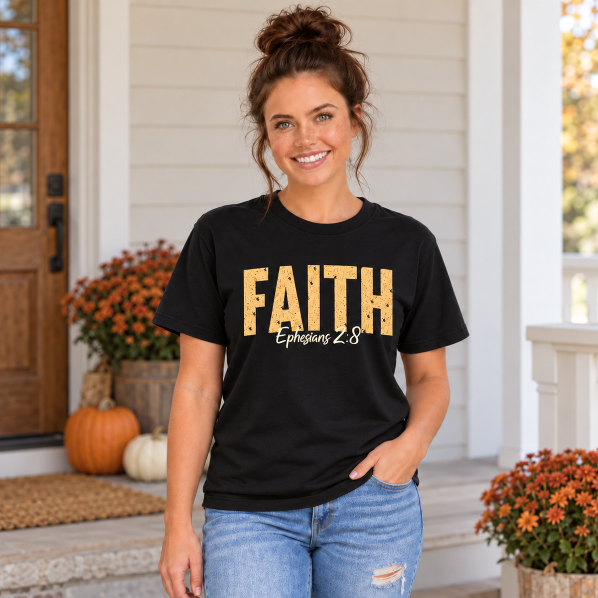 Woman modeling a black T-shirt with distressed gold FAITH text and white Ephesians 2:8 script in front of pumpkins and orange mums.