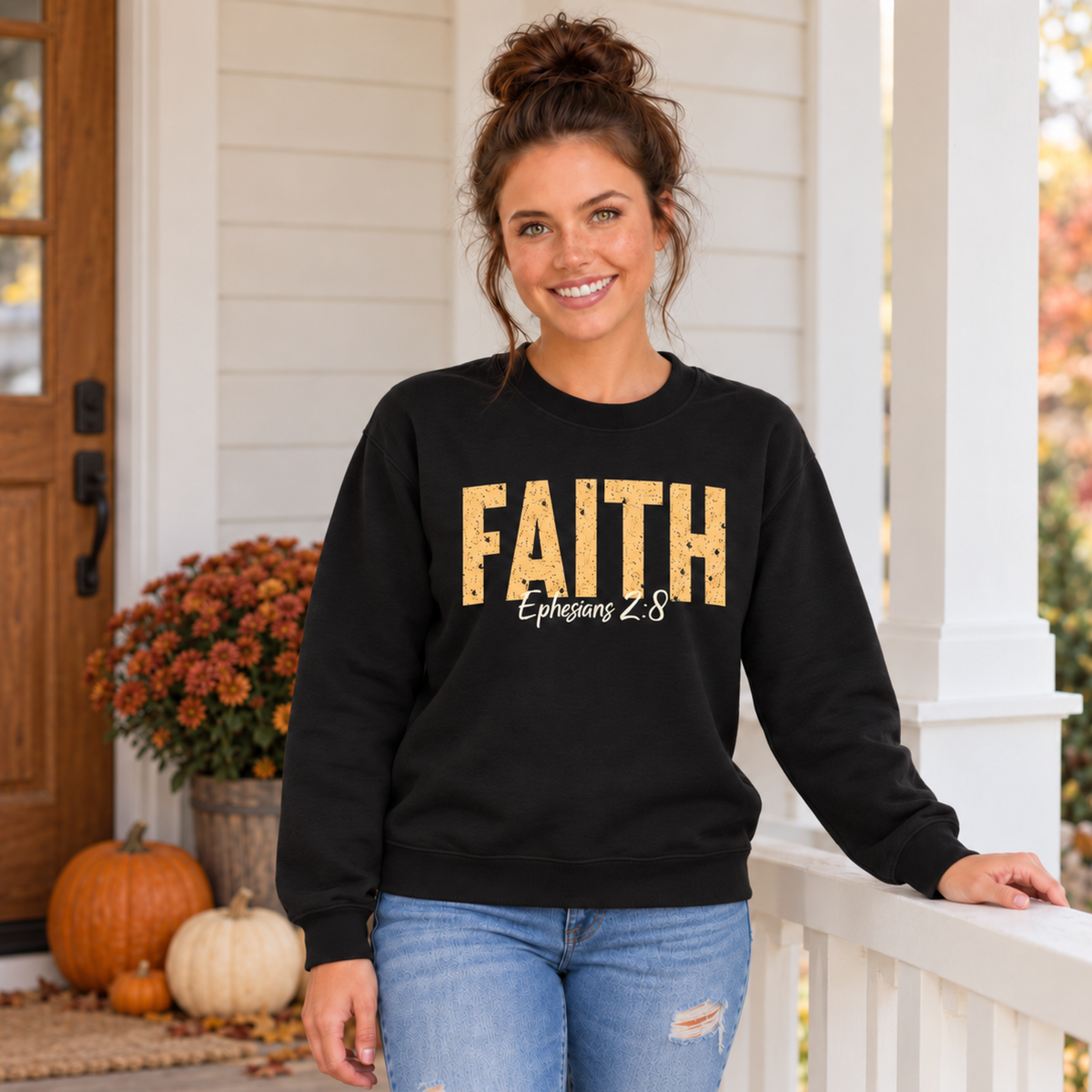 Woman wearing a black crewneck sweatshirt featuring distressed gold FAITH lettering and white Ephesians 2:8 script on an autumn porch.