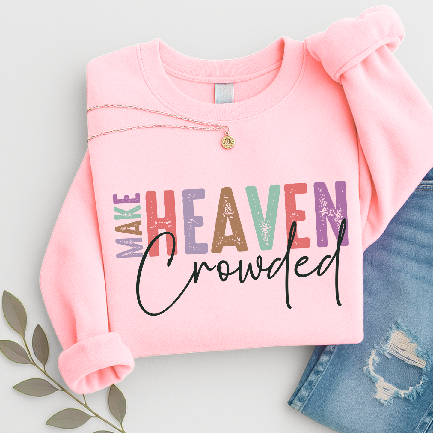 Light pink unisex sweatshirt featuring multicolor “Make Heaven Crowded” Christian faith design. Inspirational religious crewneck styled with necklace and jeans.