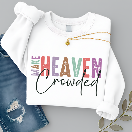 White unisex sweatshirt with colorful “Make Heaven Crowded” Christian graphic design, styled with necklace and jeans. Faith sweatshirt for women and men, inspirational religious apparel.
