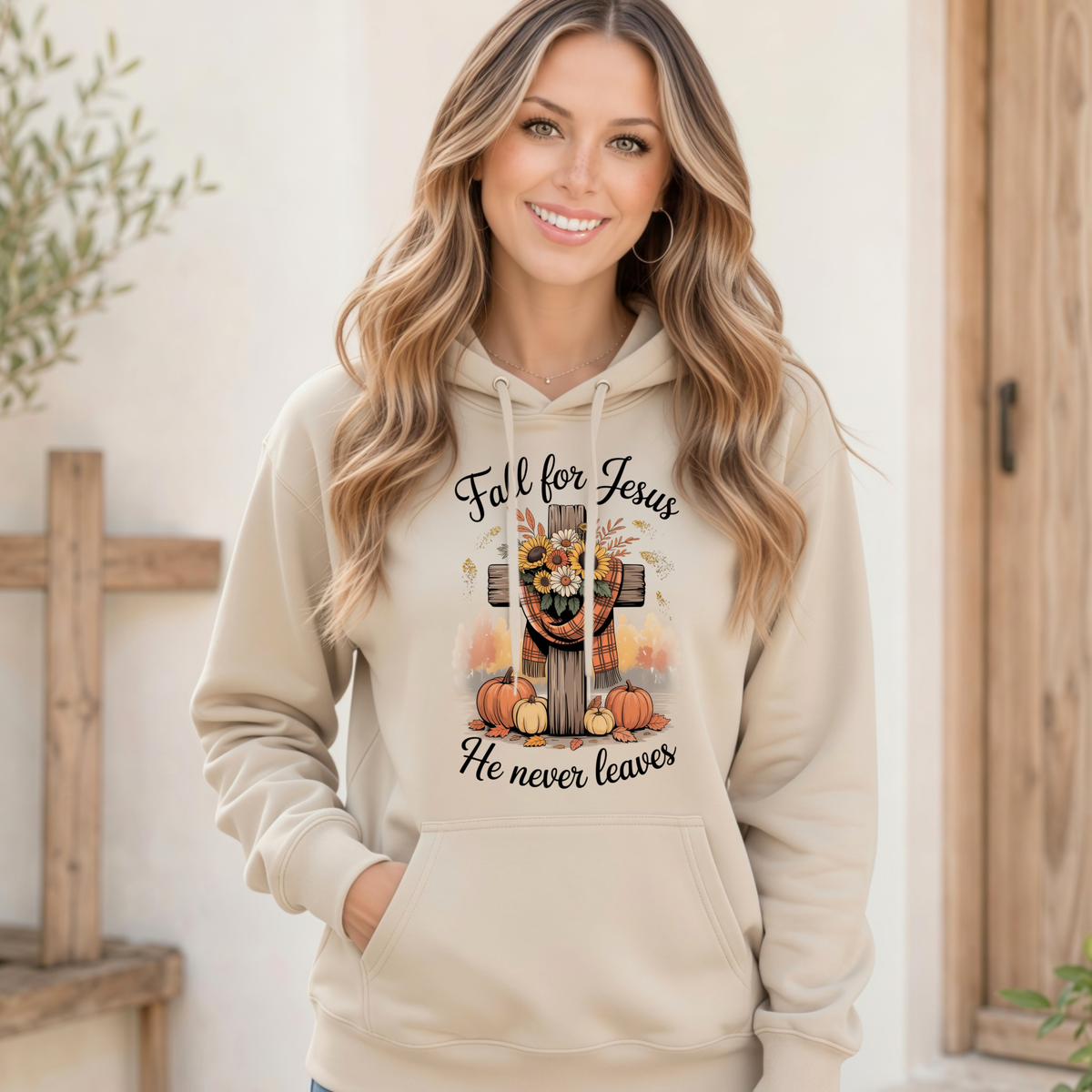 Woman wearing a Sand pullover hoodie with the Fall for Jesus He Never Leaves design featuring a cross, pumpkins, and sunflowers.