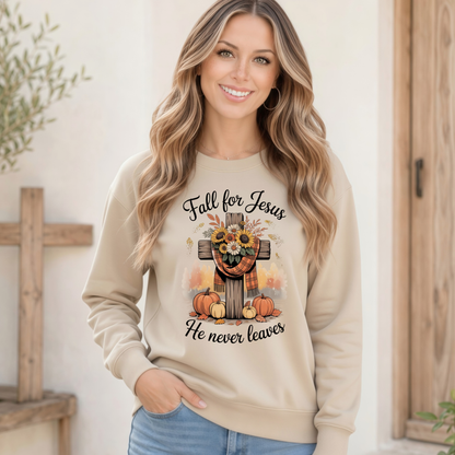 Woman wearing a Sand crewneck sweatshirt with the Fall for Jesus He Never Leaves design featuring a cross, pumpkins, and sunflowers by a rustic wooden doorway.