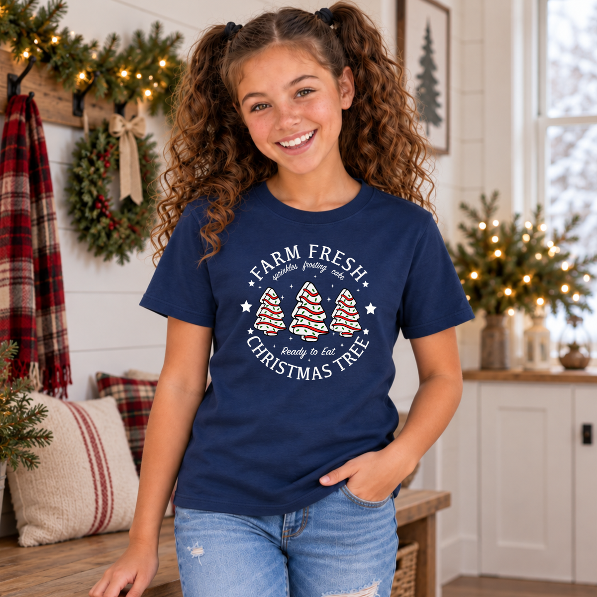 Girl wearing a navy Farm Fresh Christmas Tree Cakes T-shirt in a decorated farmhouse room.