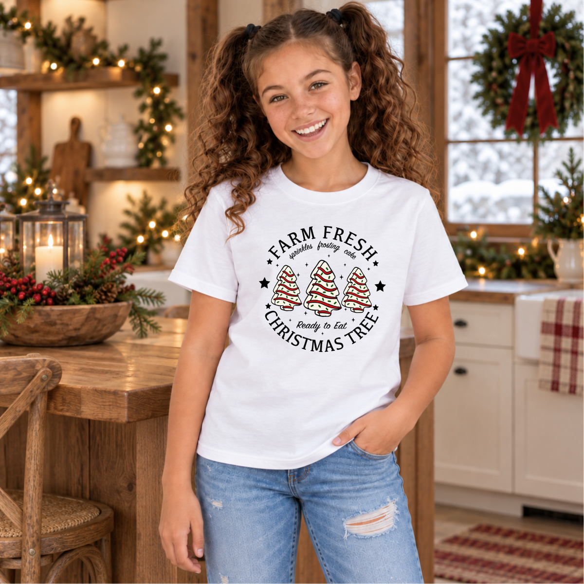 Girl modeling a white Farm Fresh Christmas Tree Cakes T-shirt in a festive kitchen.