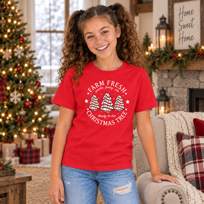 Girl modeling a red Farm Fresh Christmas Tree Cakes T-shirt beside a Christmas tree and sofa.