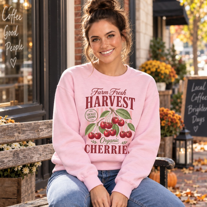 Woman seated on a bench outside a coffee shop wearing a light pink Farm Fresh Harvest Organic Cherries sweatshirt.