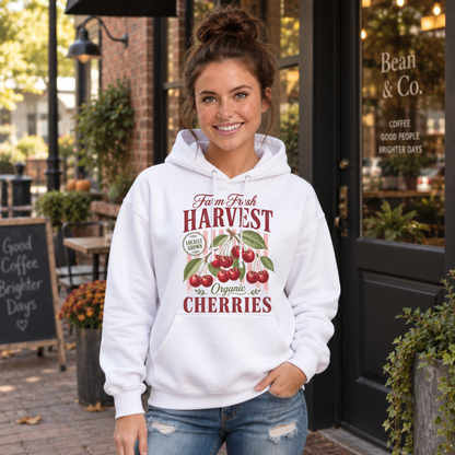 Woman wearing a white Farm Fresh Harvest Organic Cherries hoodie outside a brick coffee shop.