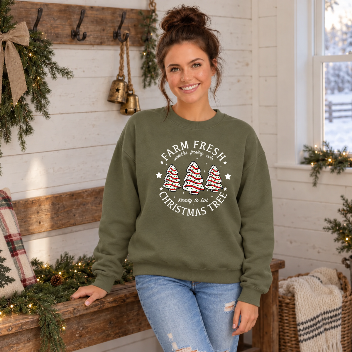 Woman wearing a military green Farm Fresh Christmas Tree Cakes sweatshirt in a farmhouse room.