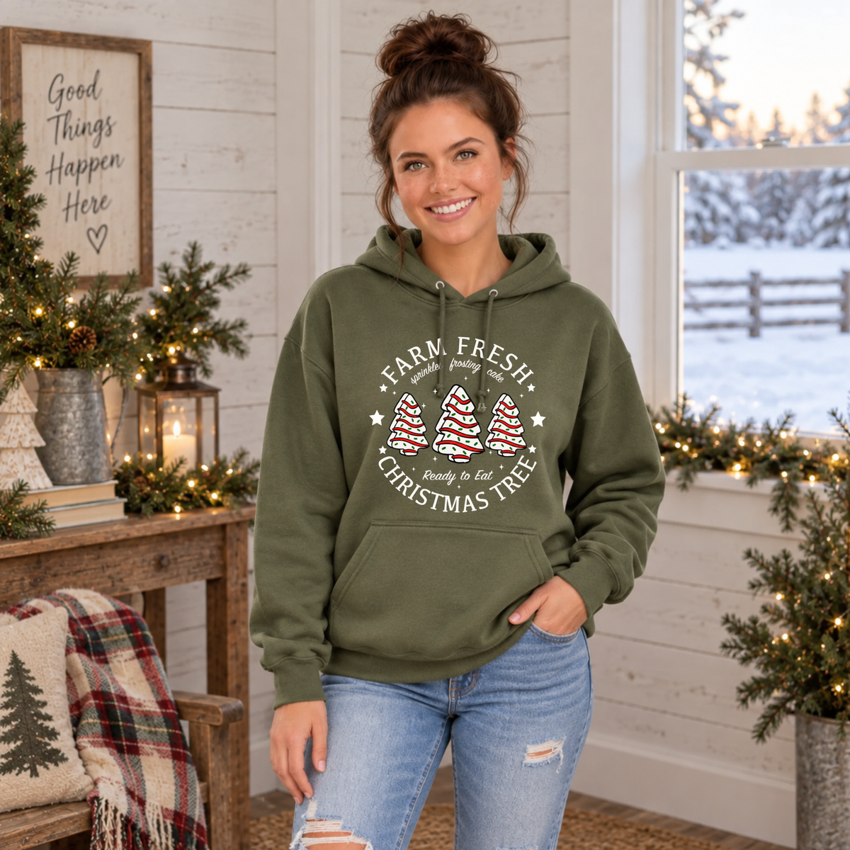 Woman wearing a military green Farm Fresh Christmas Tree Cakes hoodie in a farmhouse Christmas room.