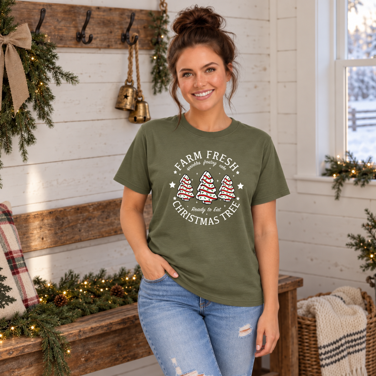 Woman modeling a military green Farm Fresh Christmas Tree Cakes T-shirt beside a decorated bench.