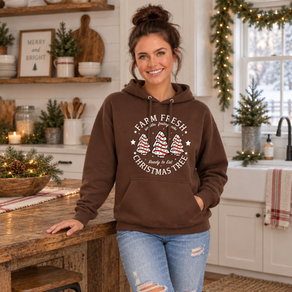 Woman in a brown Farm Fresh Christmas Tree Cakes hoodie in a holiday kitchen.