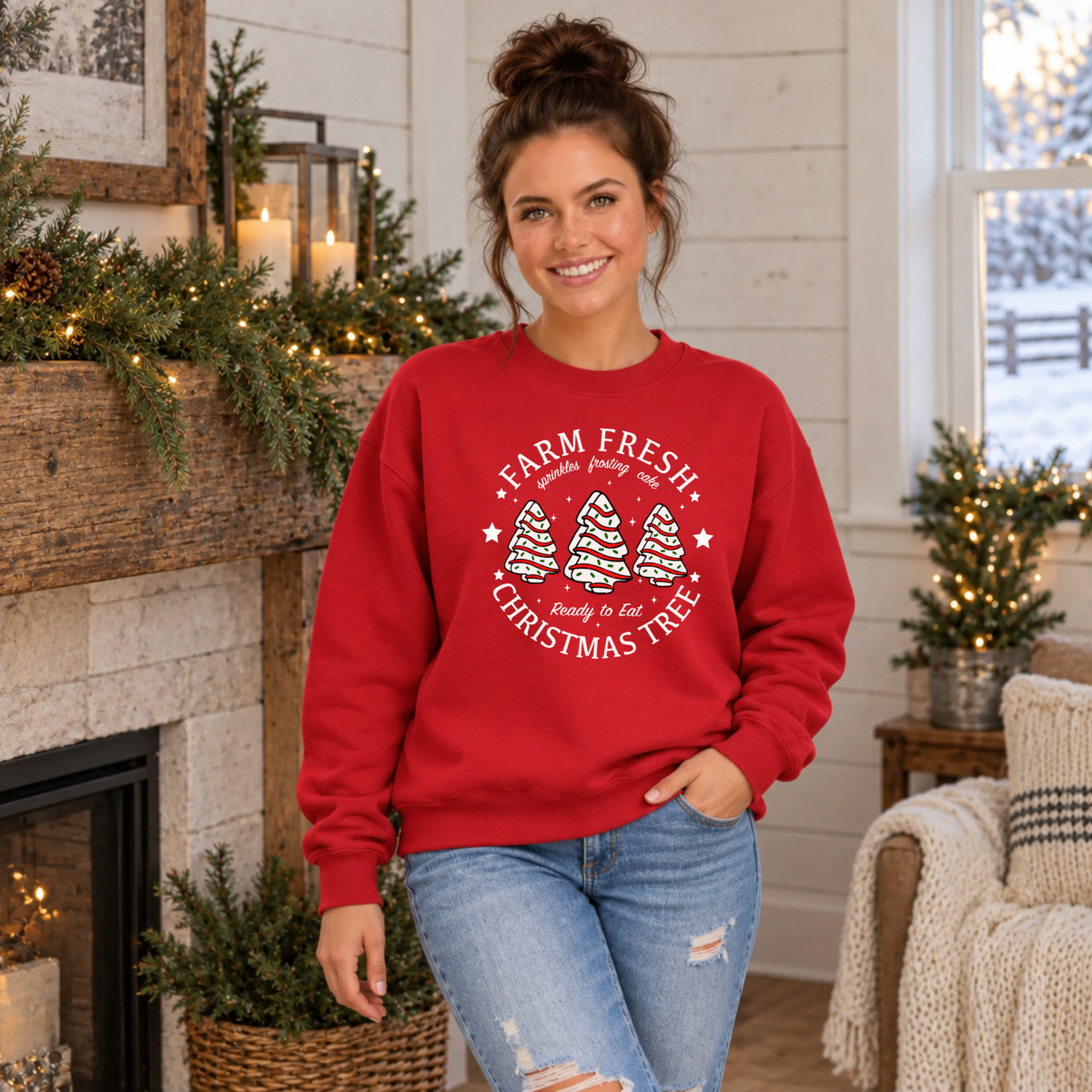 Woman modeling a red Farm Fresh Christmas Tree Cakes sweatshirt beside a holiday mantel.