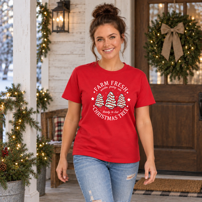 Woman wearing a red Farm Fresh Christmas Tree Cakes T-shirt outside a decorated doorway.