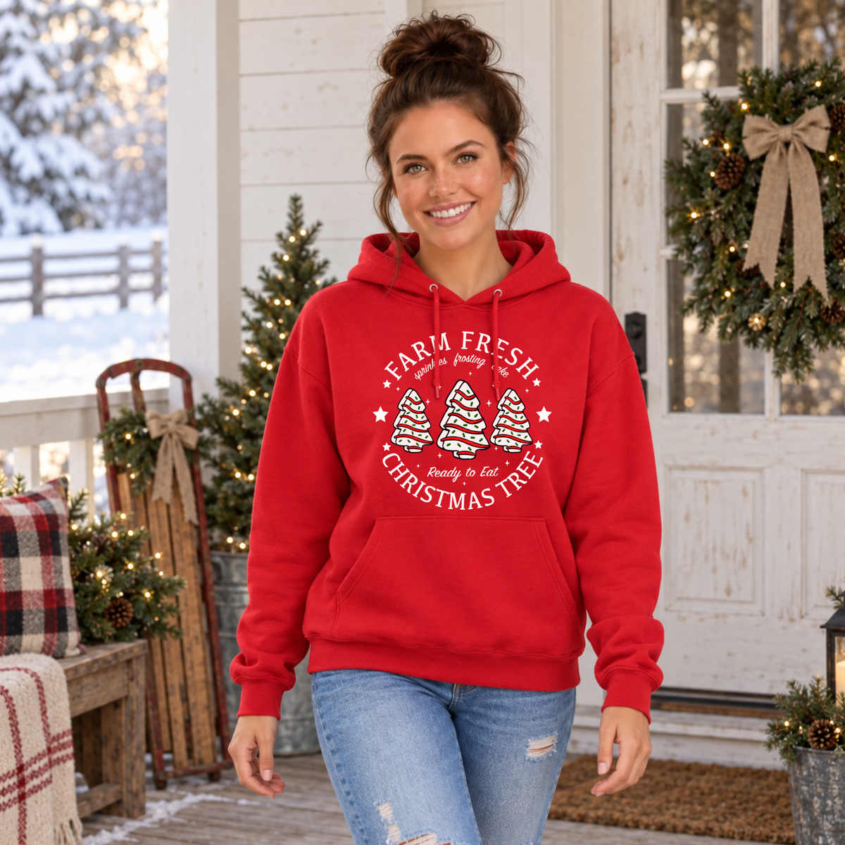 Woman modeling a red Farm Fresh Christmas Tree Cakes hoodie in a Christmas farmhouse room.