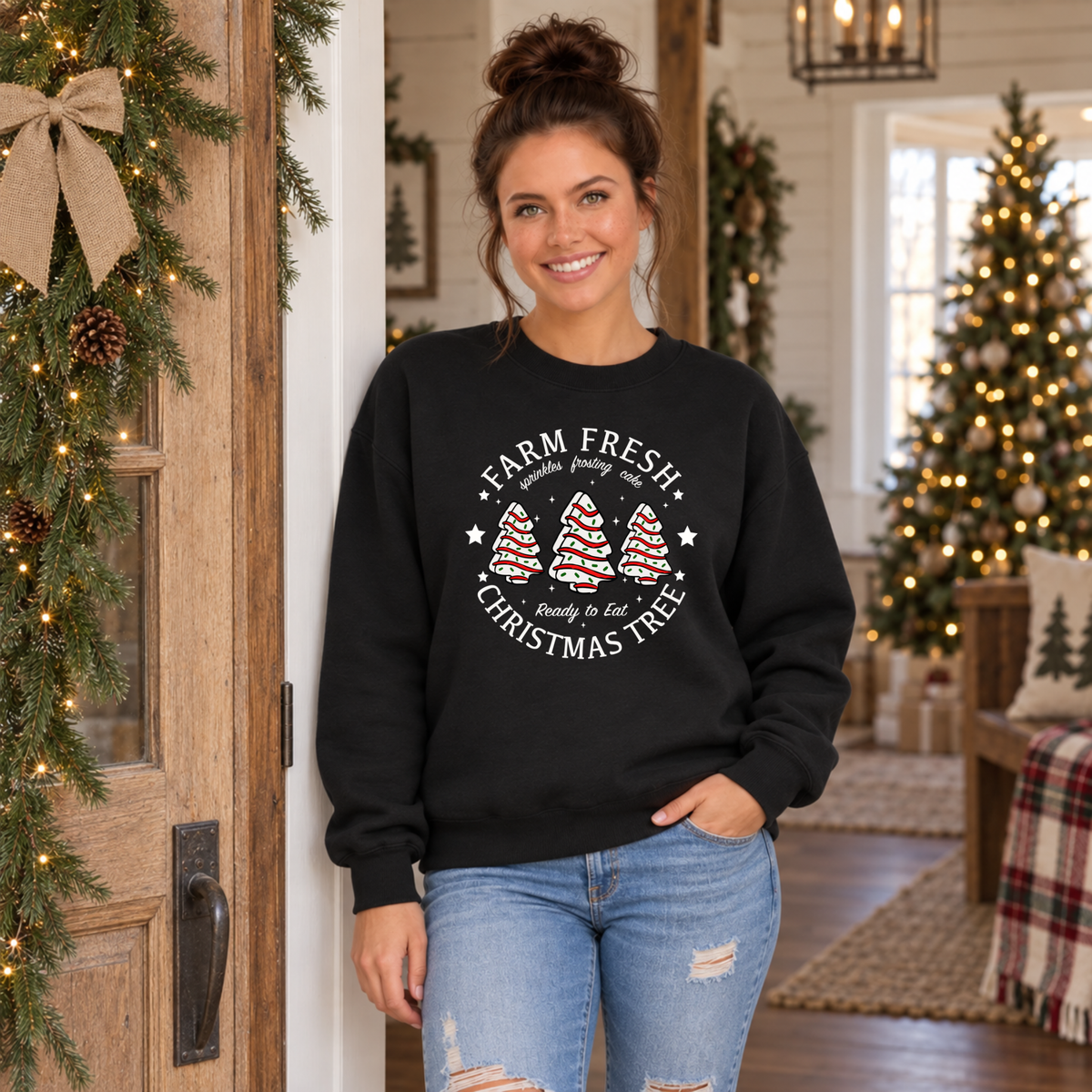 Woman modeling a black Farm Fresh Christmas Tree Cakes sweatshirt in a holiday room.