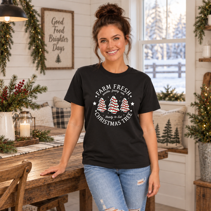 Woman wearing a black Farm Fresh Christmas Tree Cakes T-shirt by a decorated farmhouse table.