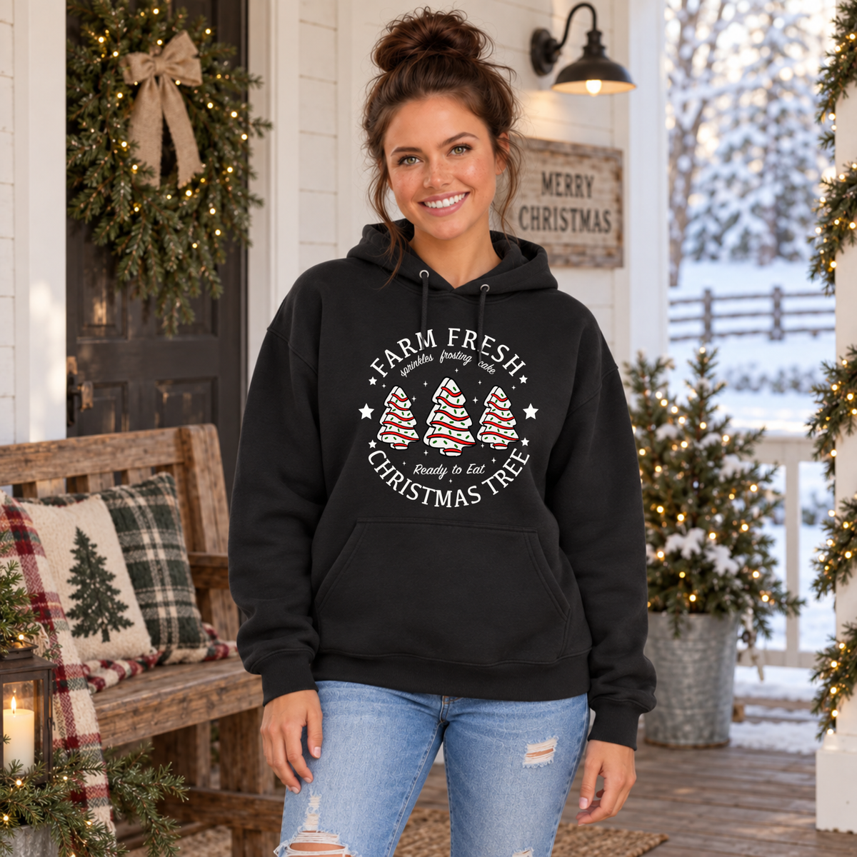Woman wearing a black Farm Fresh Christmas Tree Cakes hoodie beside a decorated bench.