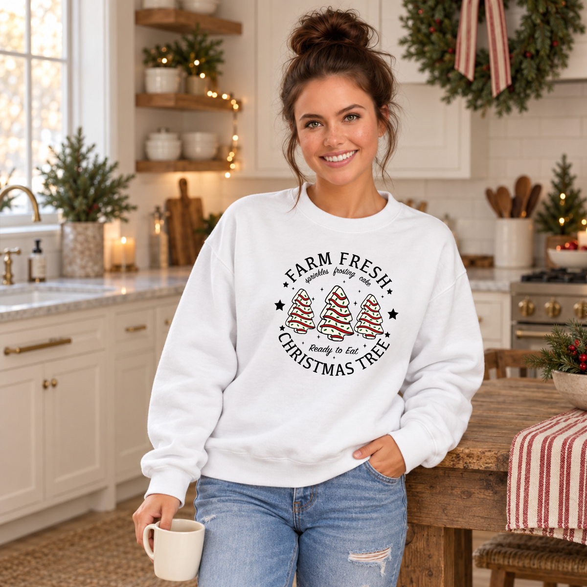 Woman wearing a white Farm Fresh Christmas Tree Cakes sweatshirt in a festive kitchen.
