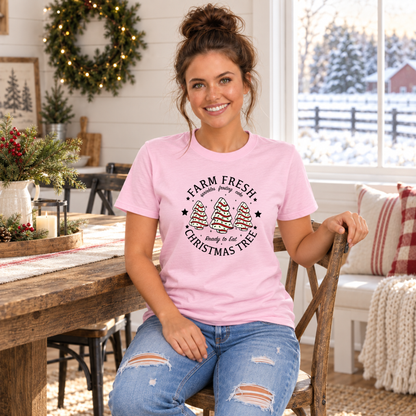 Woman seated in a light pink Farm Fresh Christmas Tree Cakes T-shirt in a holiday dining room.