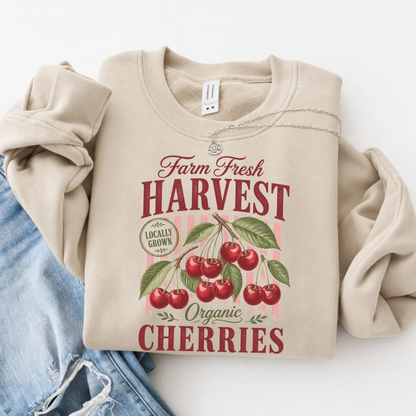 Sand crewneck sweatshirt flat lay with a vintage Farm Fresh Harvest Organic Cherries graphic, styled with blue denim on a white background.