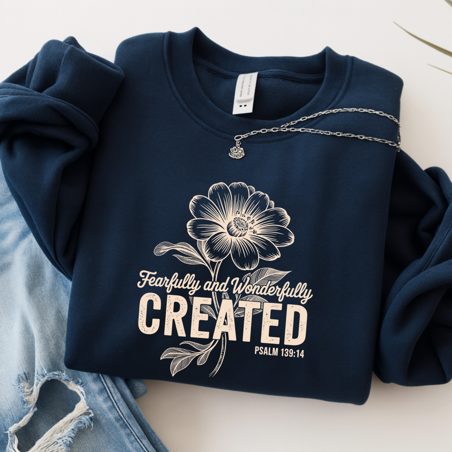 Navy blue sweatshirt with floral design and 'Fearfully and Wonderfully Created' text on a light background