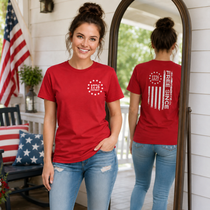 Woman in a red Free Since 1776 T-shirt standing beside a mirror showing the back distressed flag graphic on a patriotic porch