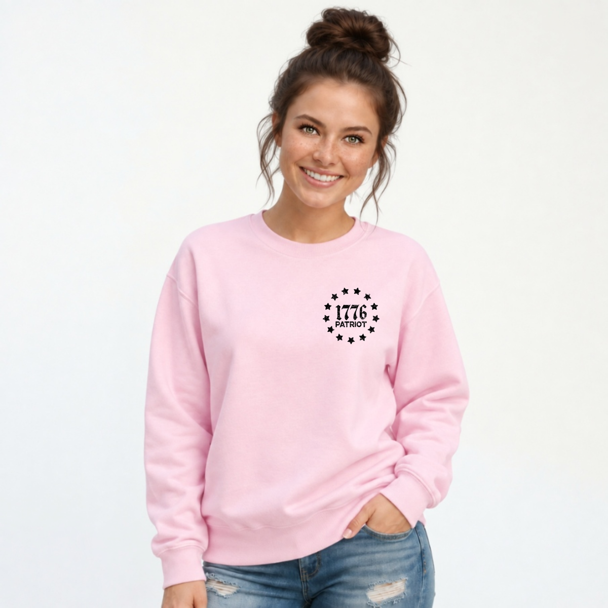 Woman wearing a light pink crewneck sweatshirt with a black 1776 Patriot emblem on the left chest