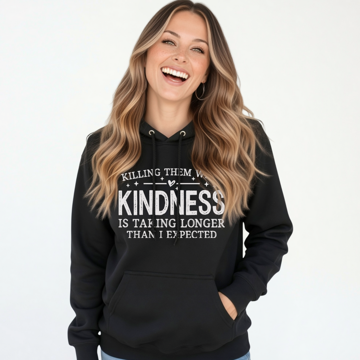 Laughing woman modeling a black Killing Them With Kindness hoodie with white lettering against a white background.
