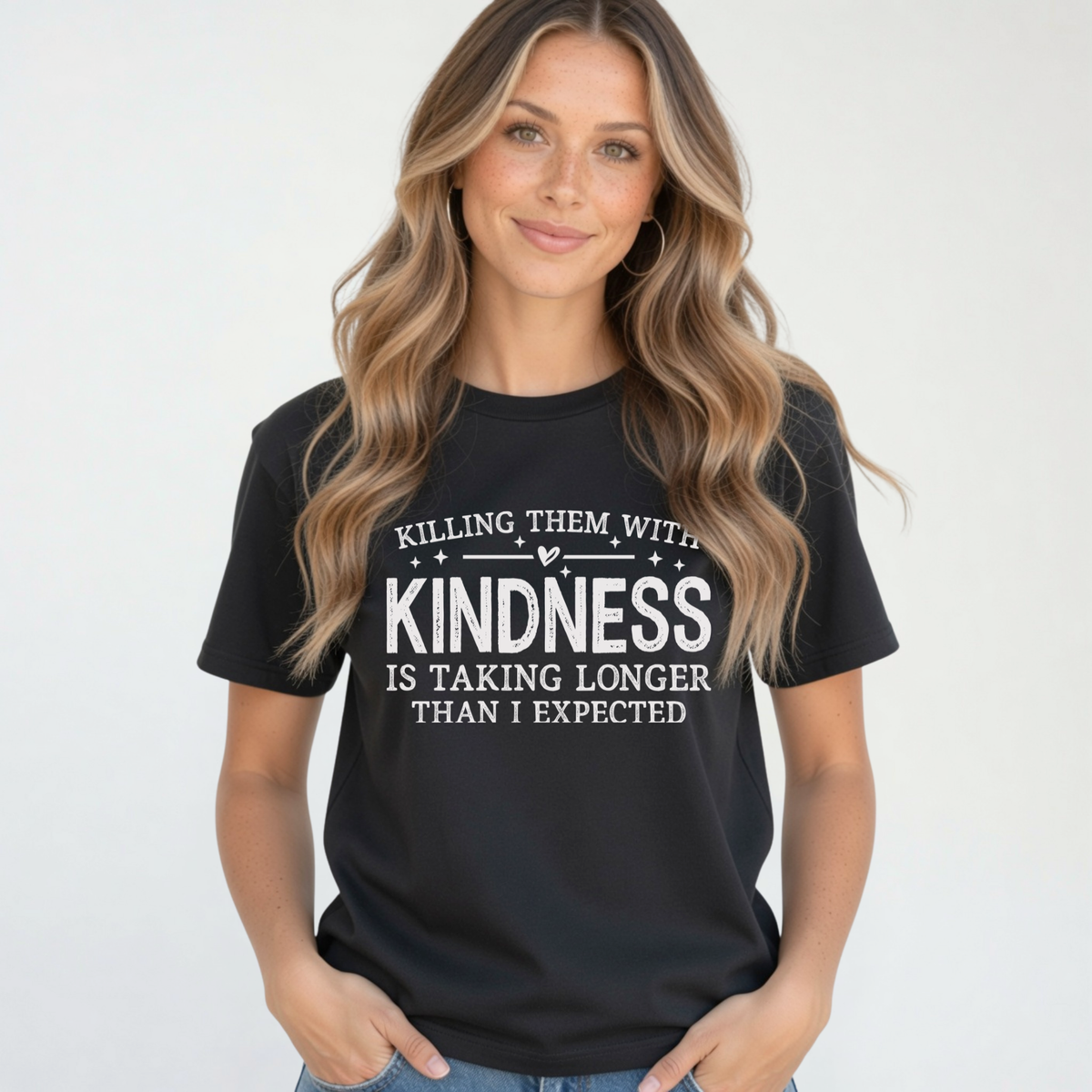 Woman modeling a black Killing Them With Kindness T-shirt with white lettering and jeans against a clean white background.