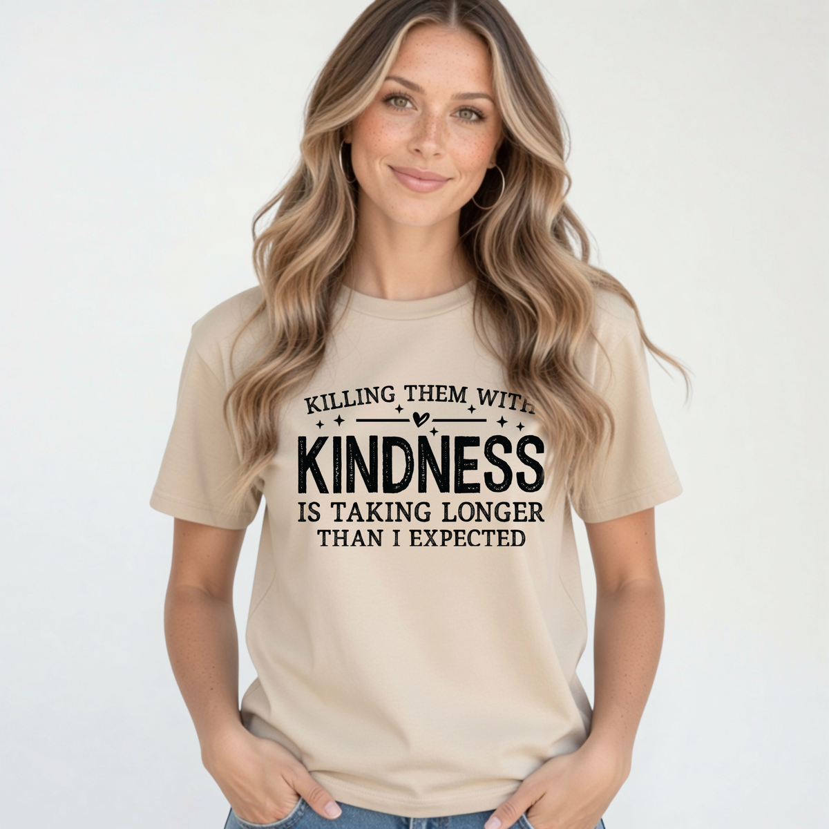 Woman modeling a sand Killing Them With Kindness T-shirt with jeans against a clean white background.
