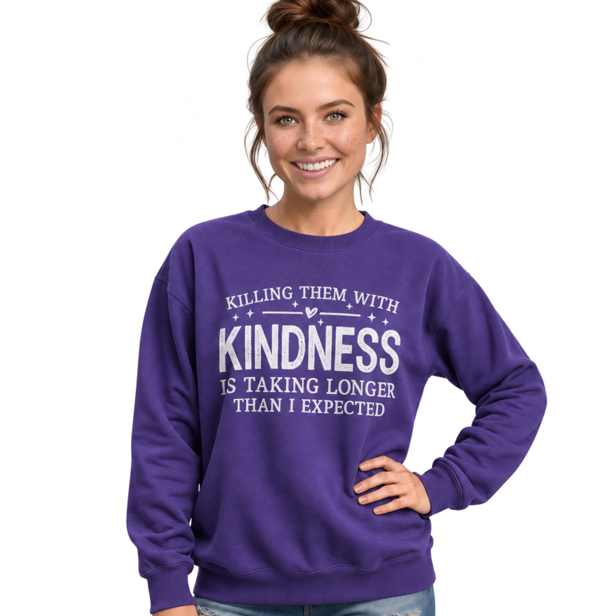 woman wearing a purple Killing Them With Kindness crewneck sweatshirt with white lettering and distressed jeans. 