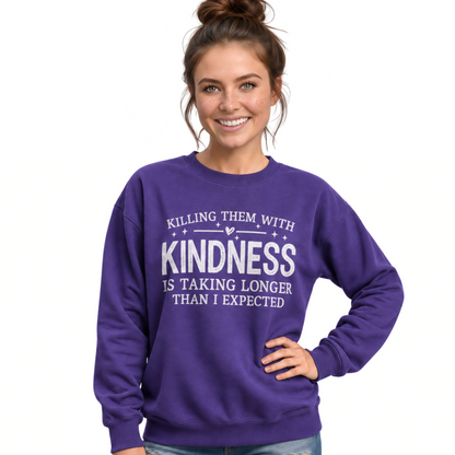 woman wearing a purple Killing Them With Kindness crewneck sweatshirt with white lettering and distressed jeans. 