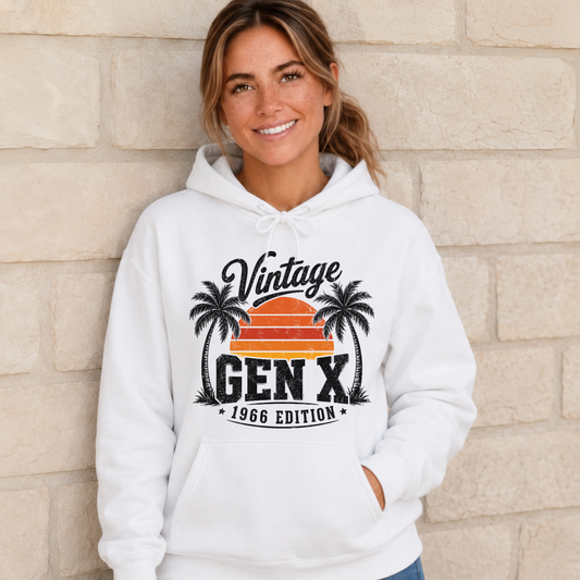 Woman wearing a white hoodie with a Vintage Gen X 1966 Edition palm-tree sunset graphic.