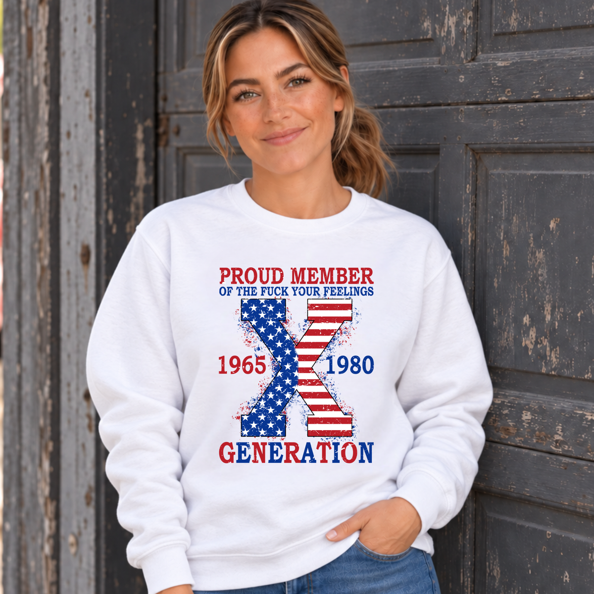 Women's white sweatshirt with patriotic Generation X 1965–1980 graphic, modeled against a rustic garage door