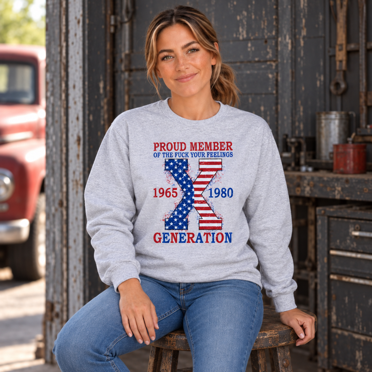 Women's sports gray sweatshirt with patriotic Generation X 1965–1980 graphic, modeled seated in a vintage garage
