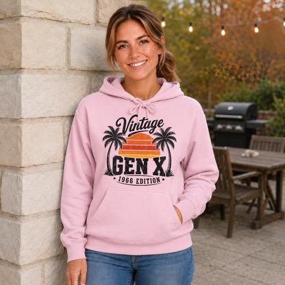 Woman wearing a light pink hoodie with a Vintage Gen X 1966 Edition palm-tree sunset graphic in a fall patio setting.