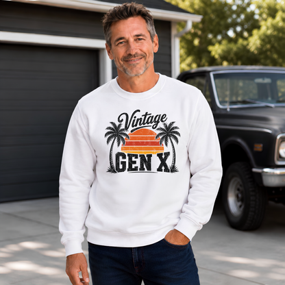 Man in a white Vintage Gen X sweatshirt with palm trees and orange sunset, standing by a garage and vintage truck.