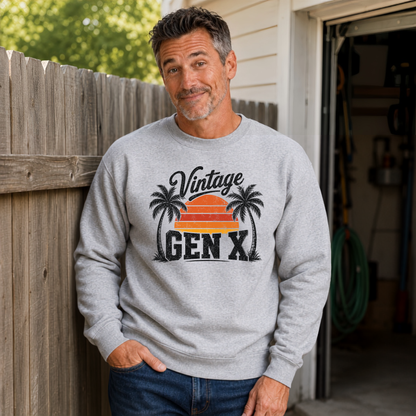 Man in a sports gray Vintage Gen X sweatshirt with orange sunset and black palm trees beside a wooden fence.