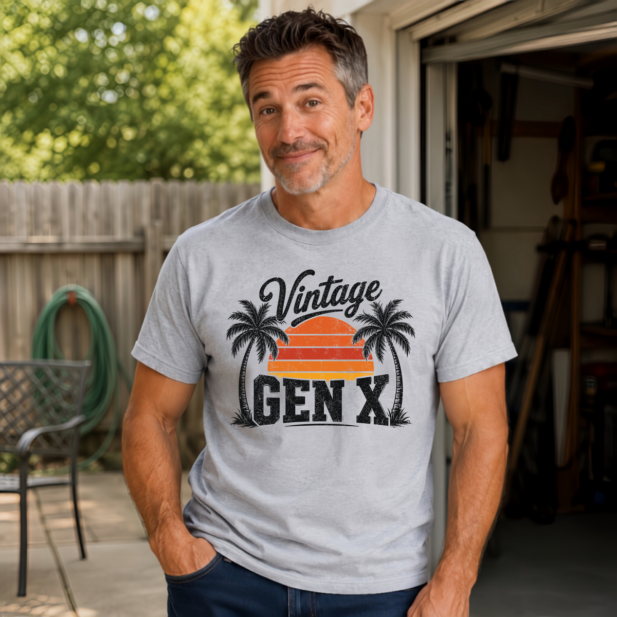 Man wearing a sports gray Vintage Gen X T-shirt with palm tree sunset graphic near an open garage.