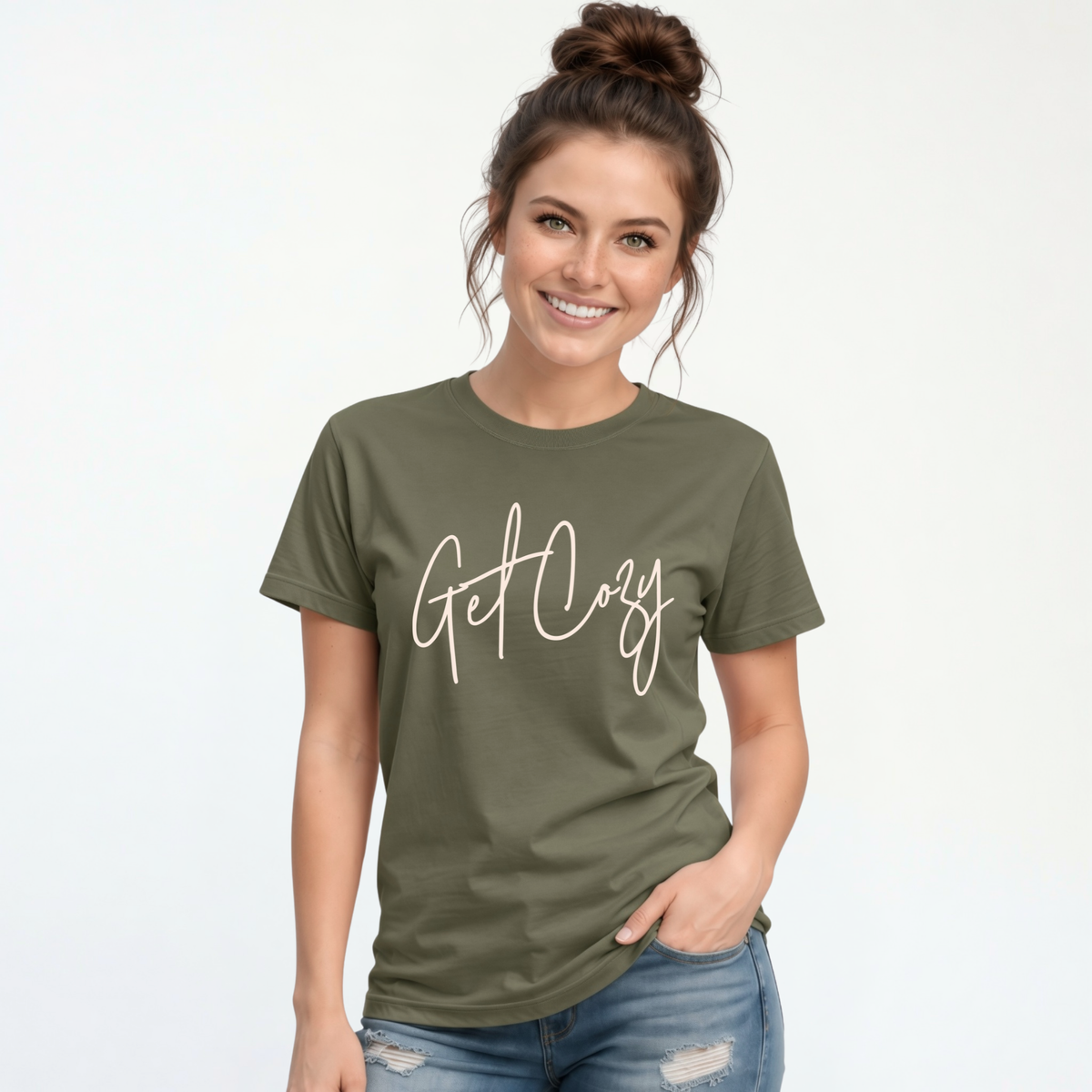Woman wearing a military green T-shirt with a minimalist Get Cozy script design, paired with distressed blue jeans on a white background.
