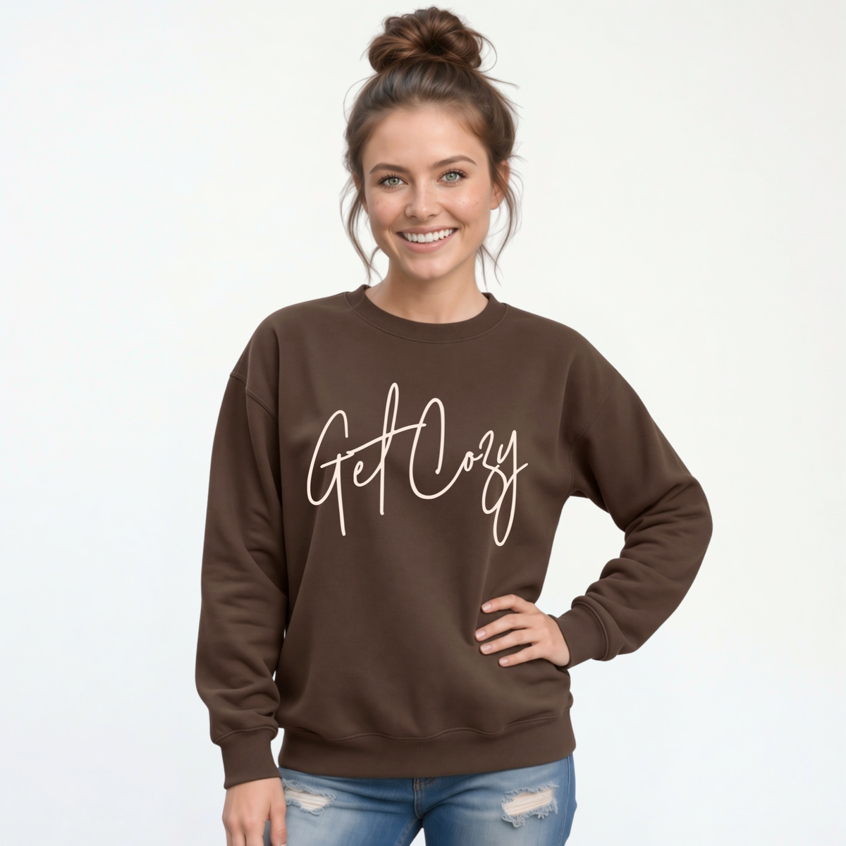 Woman wearing a brown crewneck sweatshirt with a minimalist Get Cozy script design, paired with blue jeans on a white background.