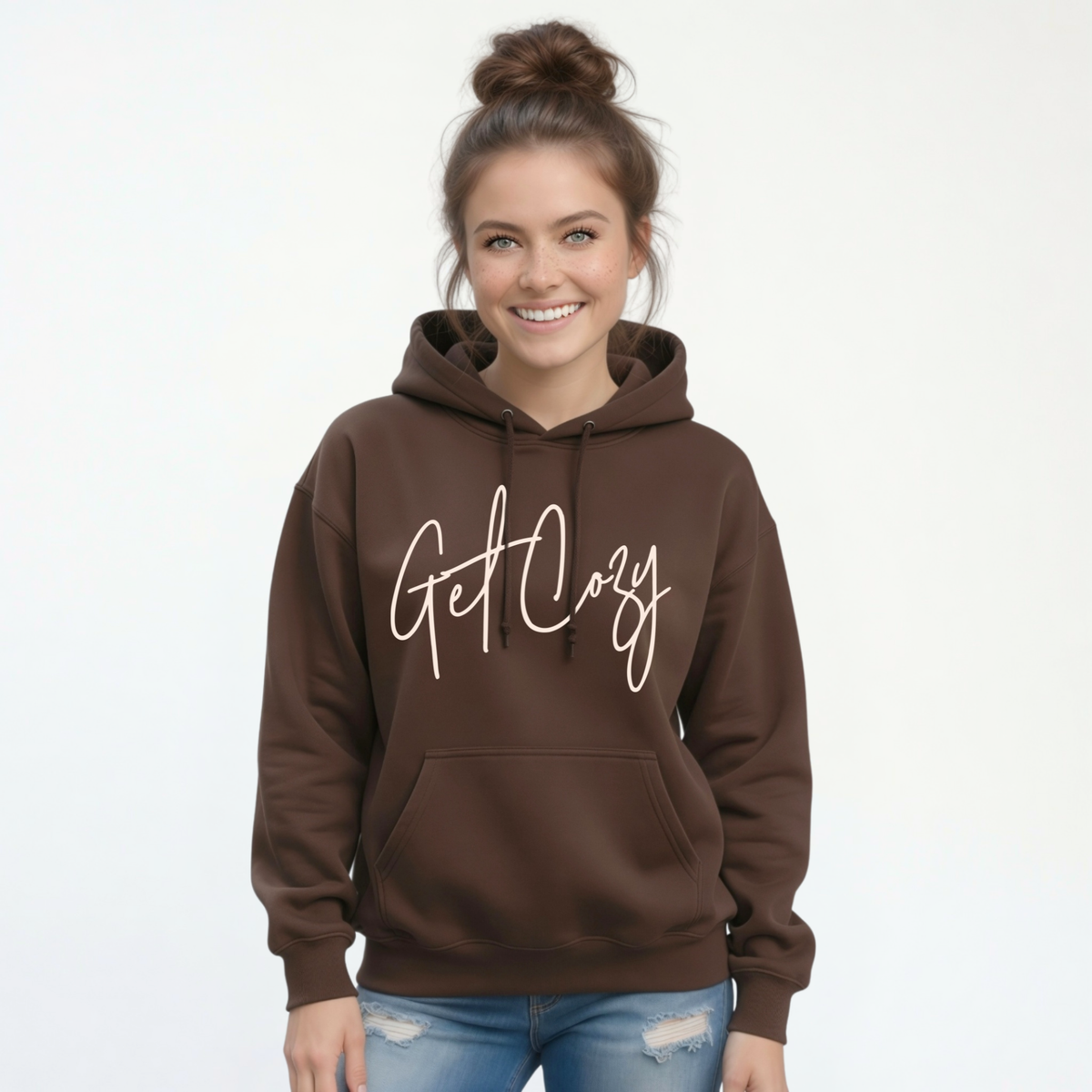 Woman wearing a brown pullover hoodie with a minimalist Get Cozy script design, paired with blue jeans on a white background.