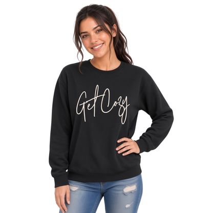 Woman wearing a black crewneck sweatshirt with a minimalist Get Cozy script design, paired with distressed blue jeans on a white background.