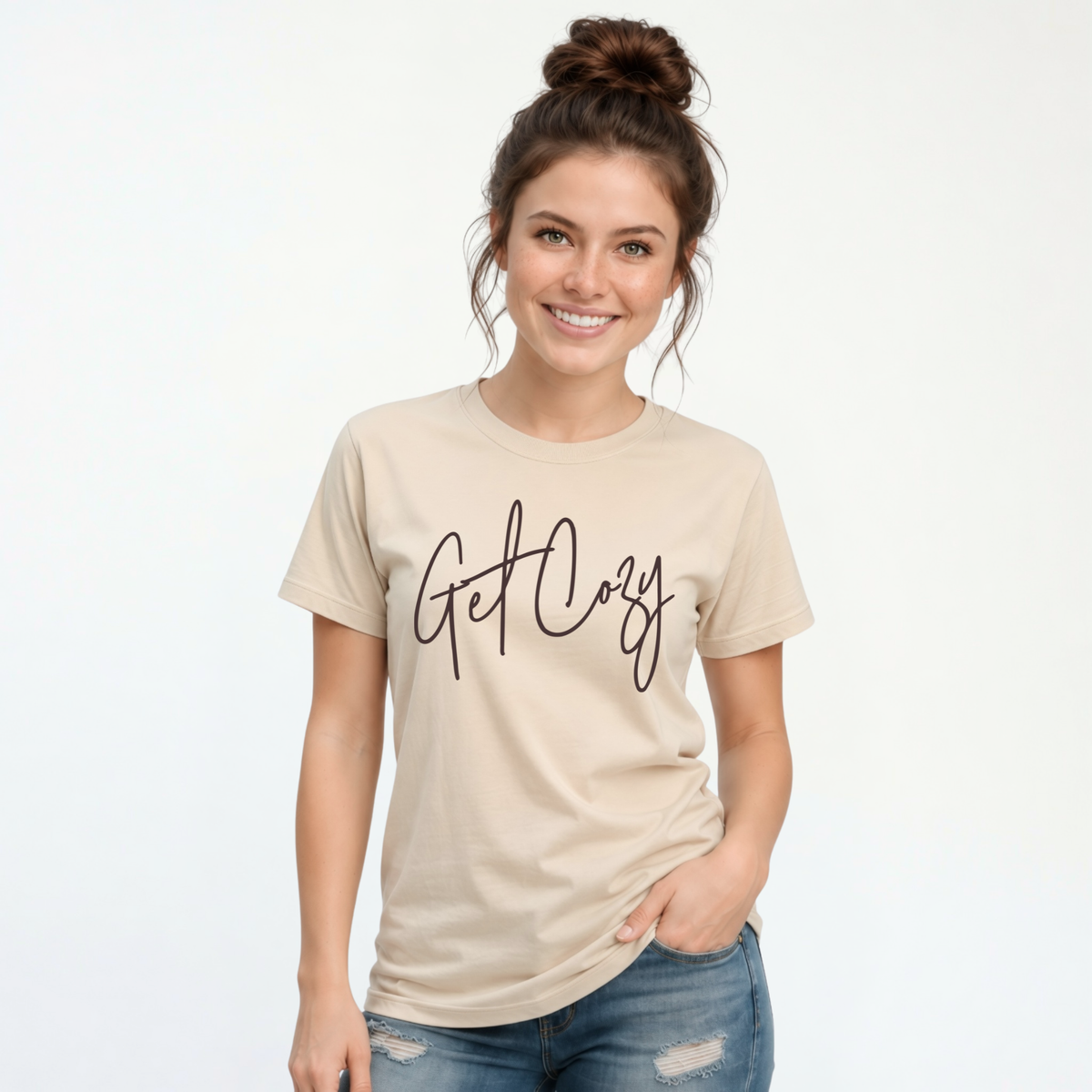 Woman wearing a sand T-shirt with a minimalist Get Cozy script design, paired with blue jeans on a white background.