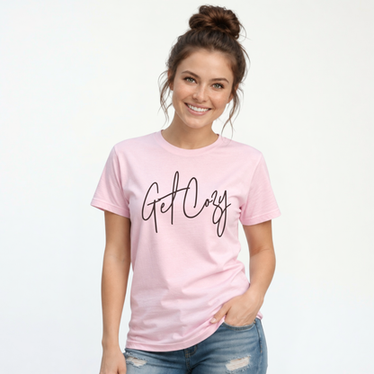 Woman wearing a light pink T-shirt with a minimalist Get Cozy script design, paired with distressed blue jeans on a white background.