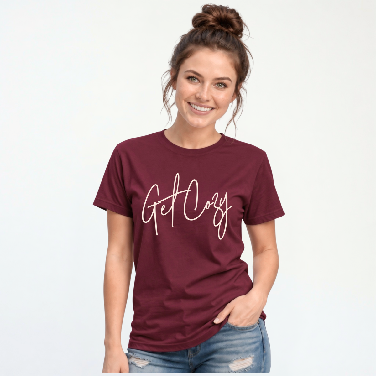 Woman wearing a maroon T-shirt with a minimalist Get Cozy script design, paired with blue jeans on a white background.
