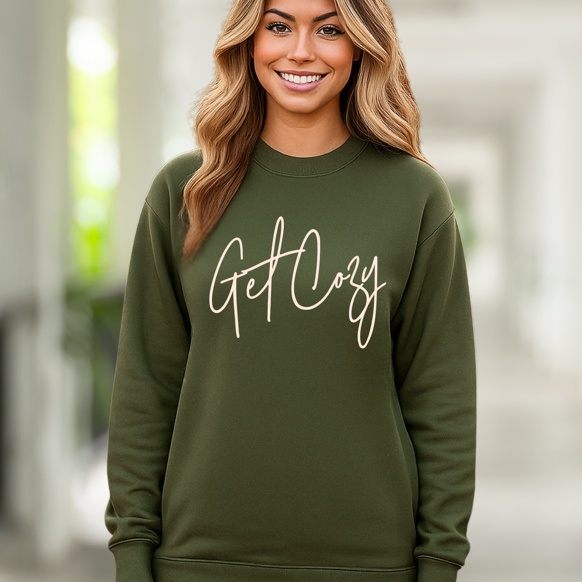 Woman wearing a green sweatshirt with 'Get Cozy' text against a blurred background