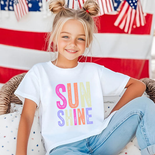 Girl in white “Sunshine” shirt with flags in background

